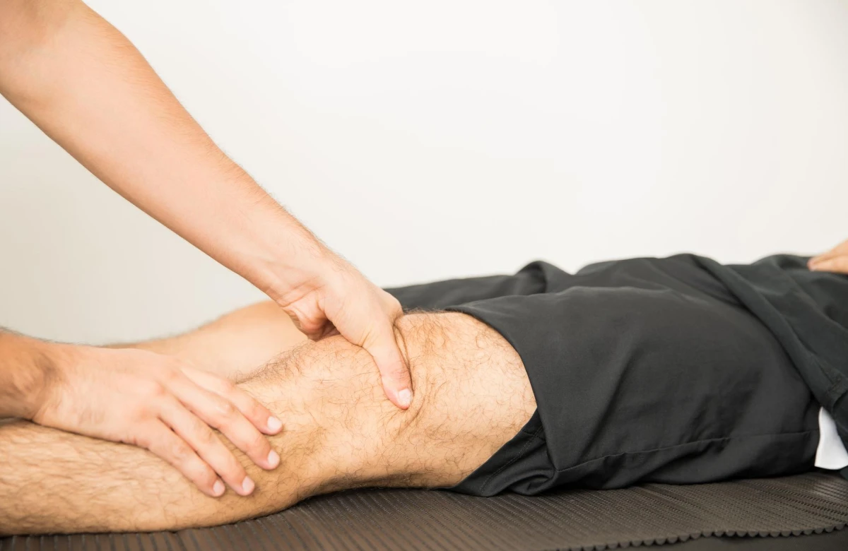 Fisioterapeuta mobilizando o joelho de um homem deitado na maca.