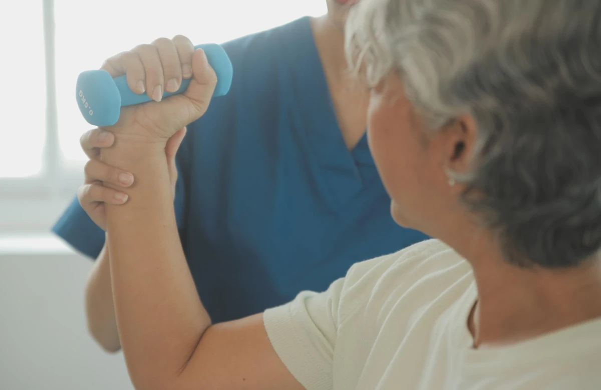 Fisioterapeuta apoiando o braço de uma senhora durante exercício com halter.